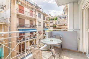 A balcony with a round table and two wicker chairs, surrounded by a metal railing. - Modern Athens Apartment Near Metro Station (Athens)