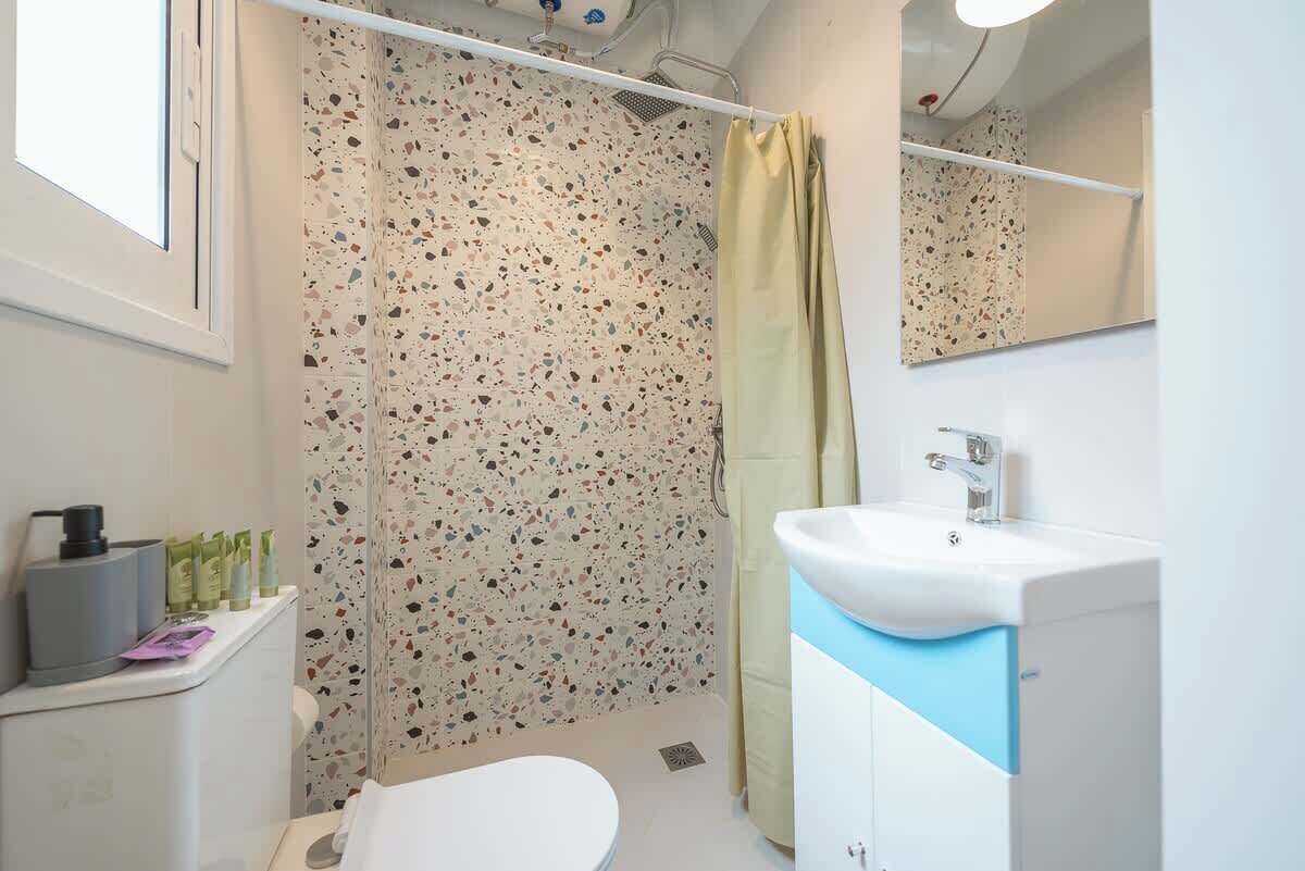 Un baño con lavamanos blanco, un espejo, cortina de ducha y artículos de tocador en un estante.