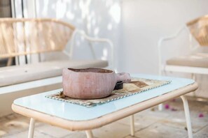 Ein hellblauer Tisch mit einer pinkfarbenen Keramiktasse und einem kleinen schwarzen Behälter auf einer gewebten Tischunterlage.