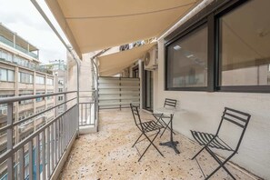 Ein Balkon mit Tisch und Stühlen, ein großes Fenster und Blick auf angrenzende Gebäude.
