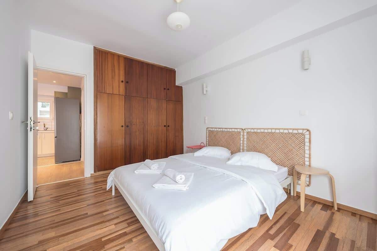 A bedroom with a large bed, wooden wardrobe, and a small bedside table.