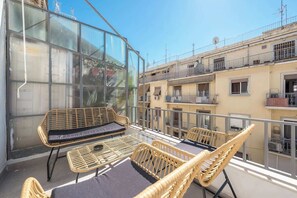 Ein Balkon mit Korbmöbeln und einer Glaswand mit Blick auf ein Wohngebiet.