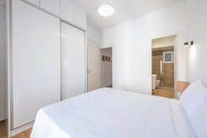 Ein Schlafzimmer mit einem großen Bett, einem Kleiderschrank und einem durchgehenden Türrahmen sichtbaren Badezimmer.