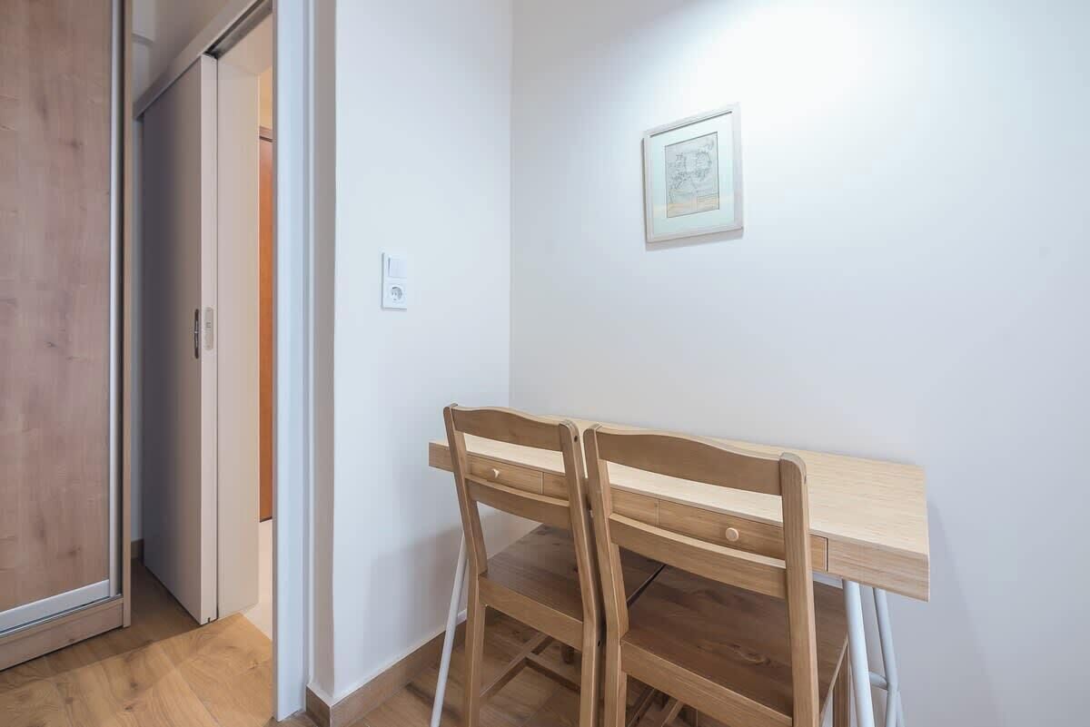 A room with a wooden desk and chairs, a framed picture on the wall, and a door leading to another room.