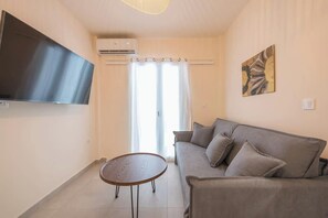 A living room with a sofa, a coffee table, a flat-screen TV, an air conditioning unit, and a painting on the wall. - Zen Euphoria, Exarchia (Athens)