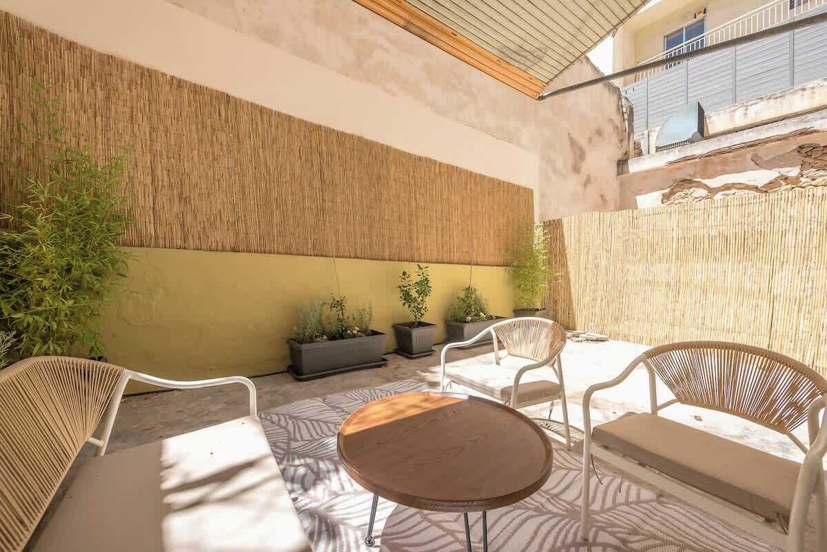 A sunlit patio with wicker furniture, potted plants, and a textured wall.