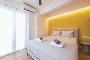 A hotel room with a bed, a bedside table, a window with curtains, and an air conditioning unit. - Zen Euphoria, Exarchia (Athens)