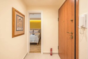 A hallway leading to a bedroom with a bed, a framed picture on the wall, a wooden door, and a fire extinguisher. - Zen Euphoria, Exarchia (Athens)