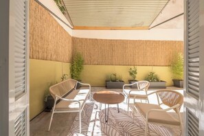 A sunlit patio with a seating area, including a table and chairs, surrounded by potted plants and a bamboo wall. - Zen Euphoria, Exarchia (Athens)