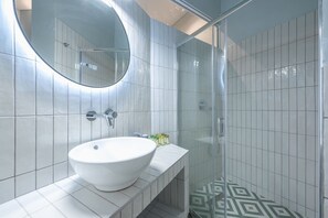 Een moderne badkamer met een groot ovaal wastafel, een ronde spiegel en een douchecabine met glazen wanden.