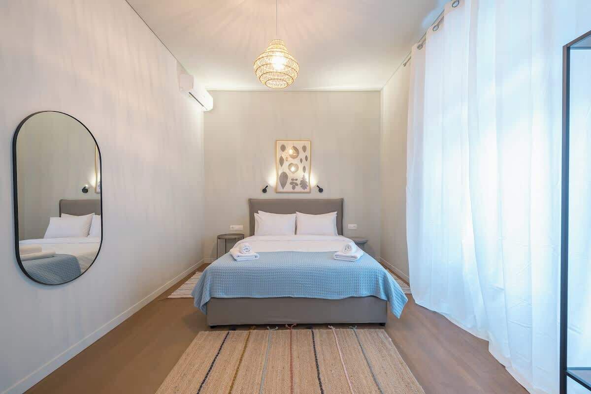 A bedroom with a bed, a mirror, a bedside table, a hanging light fixture, and a wall-mounted artwork.