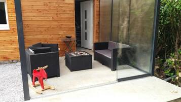 Un área de estar moderna al aire libre con sofás y una mesita, una terraza de madera y una puerta de cristal que da a un jardín.