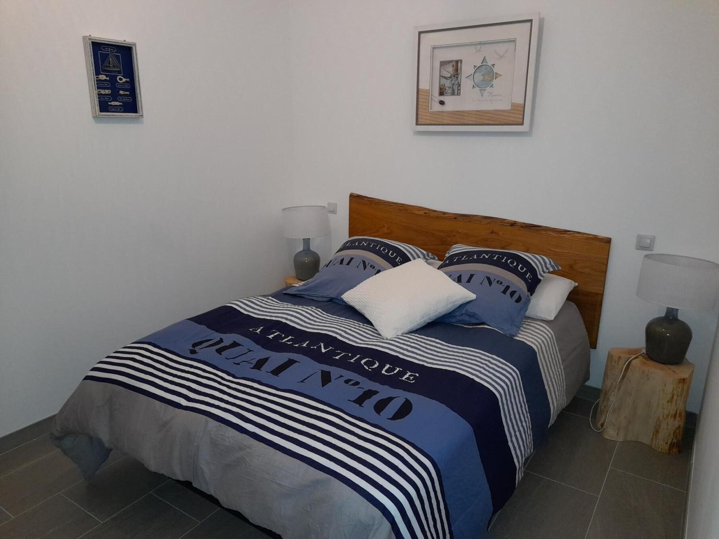 Un lit avec une couvre-lit à rayures et des coussins assortis, une tête de lit en bois, des lampes de chevet et un tableau encadré au mur.
