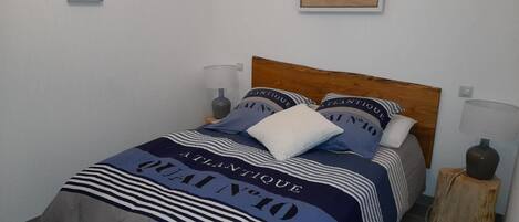 Una cama con colcha y almohadas a rayas, un cabecero de madera, lámparas de noche y un cuadro en la pared.