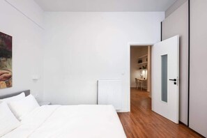 A bedroom with a bed, a radiator, a door leading to a hallway, and a painting on the wall. - Central Athens Exarchia Apartment w/ Balcony (Athens)