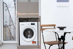 A compact room with a washing machine, a small table, and a chair. - Central Athens Exarchia Apartment w/ Balcony (Athens)