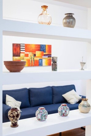 A room with a blue sofa, decorative vases, and a colorful abstract painting on the wall. - Central Athens Exarchia Apartment w/ Balcony (Athens)