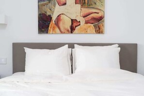 Ein Bett mit weißer Bettwäsche und Kissen, ein grauer Kopfteil und ein Bild an der Wand.