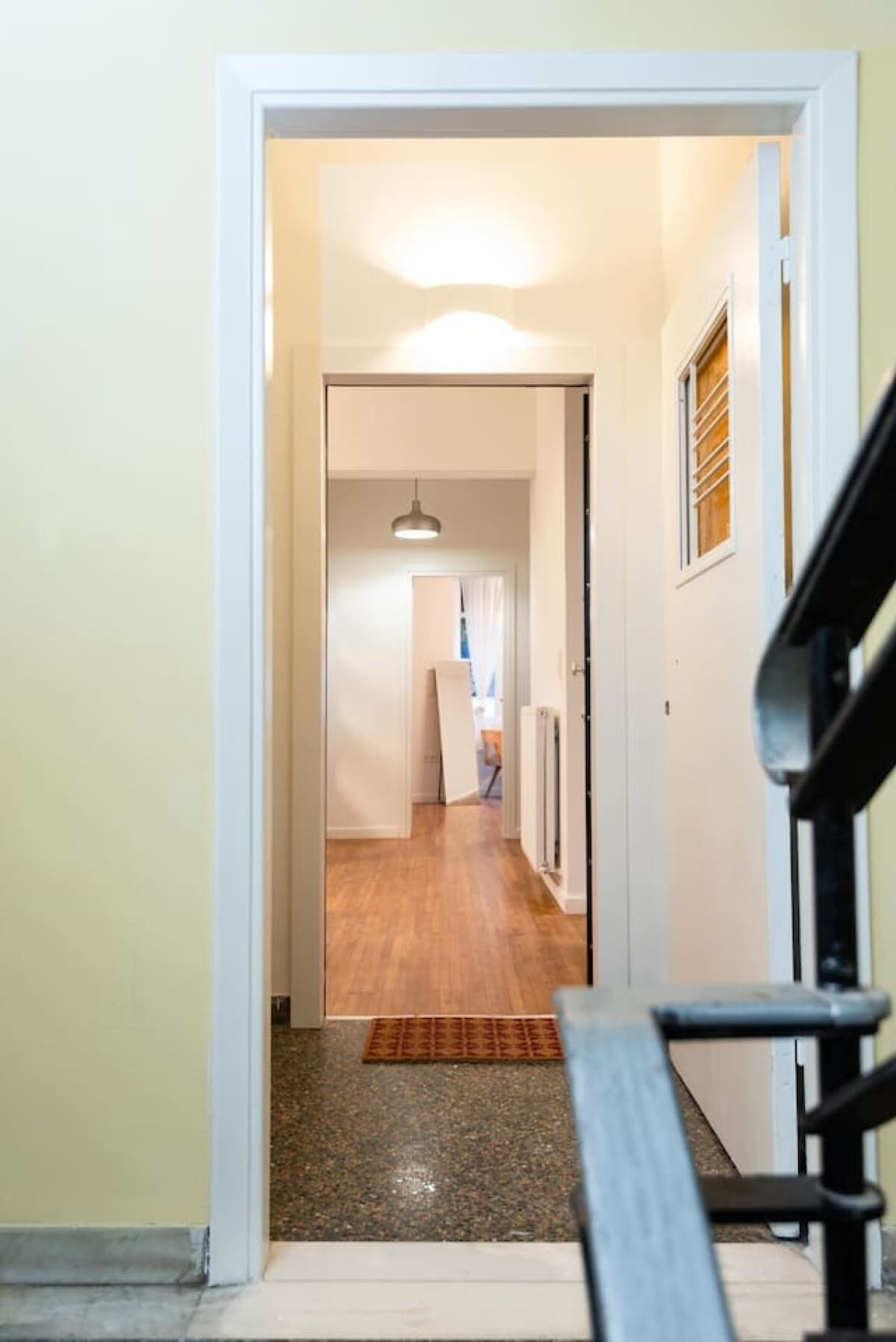 A hallway with a wooden floor, a bench, and a door leading to another room.