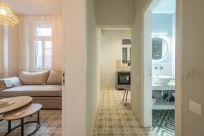 Ein modernes Interieur mit einer Couch, einem runden Tisch, einem gemusterten Boden und Blick in ein Badezimmer mit Waschbecken und Spiegel.