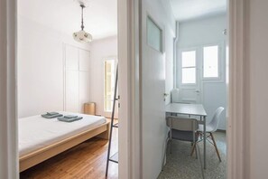 A room with a bed, a desk, and a chair, with a window and a door visible. - Modern Exarcheia Apt w/Balcony, Walk to Cafes & (Athens City)