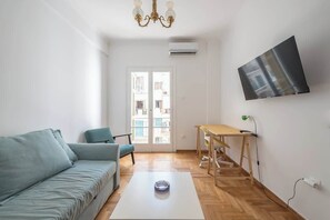 A modern living room with a sofa, a coffee table, a TV mounted on the wall, and a window with a view of buildings. - Modern Exarcheia Apt w/Balcony, Walk to Cafes & (Athens City)