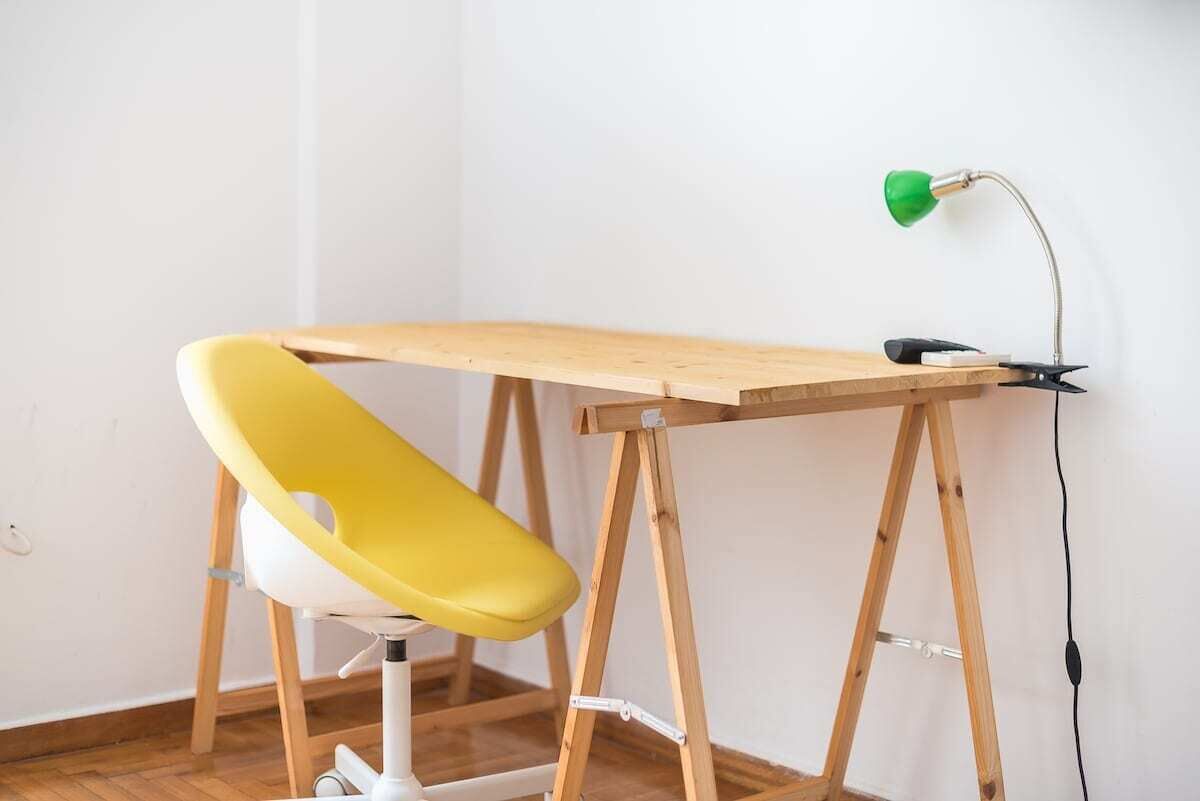 Un espace de travail avec un bureau en bois, une chaise jaune et une lampe de bureau verte.