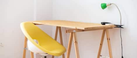 Un espace de travail avec un bureau en bois, une chaise jaune et une lampe de bureau verte.