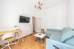 A modern living room with a flat-screen TV, a desk with a chair, a light blue sofa, and a chandelier. - Modern Exarcheia Apt w/Balcony, Walk to Cafes & (Athens City)