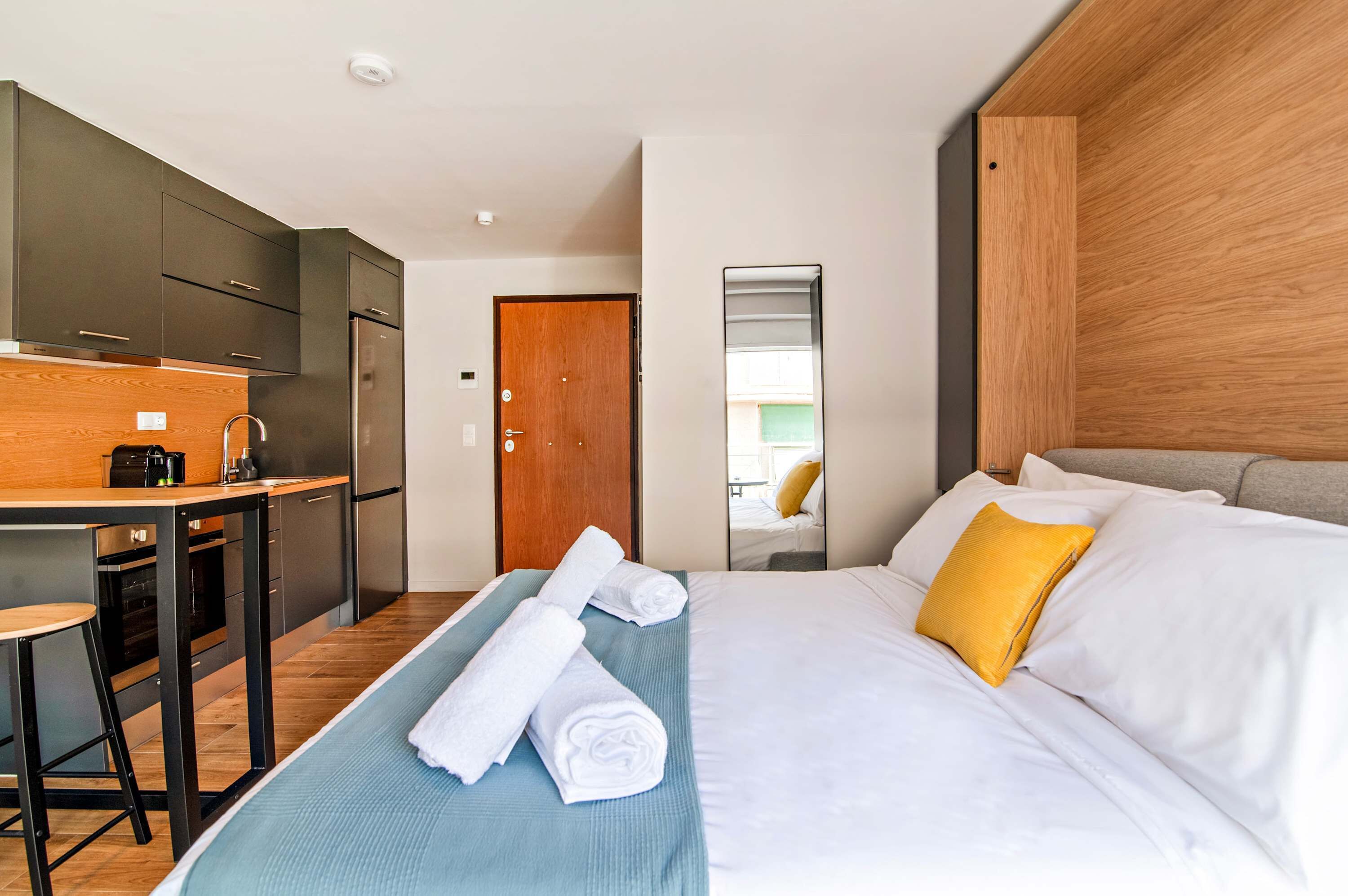 Een hotelkamer met een bed, bureau, kitchenette en spiegel.