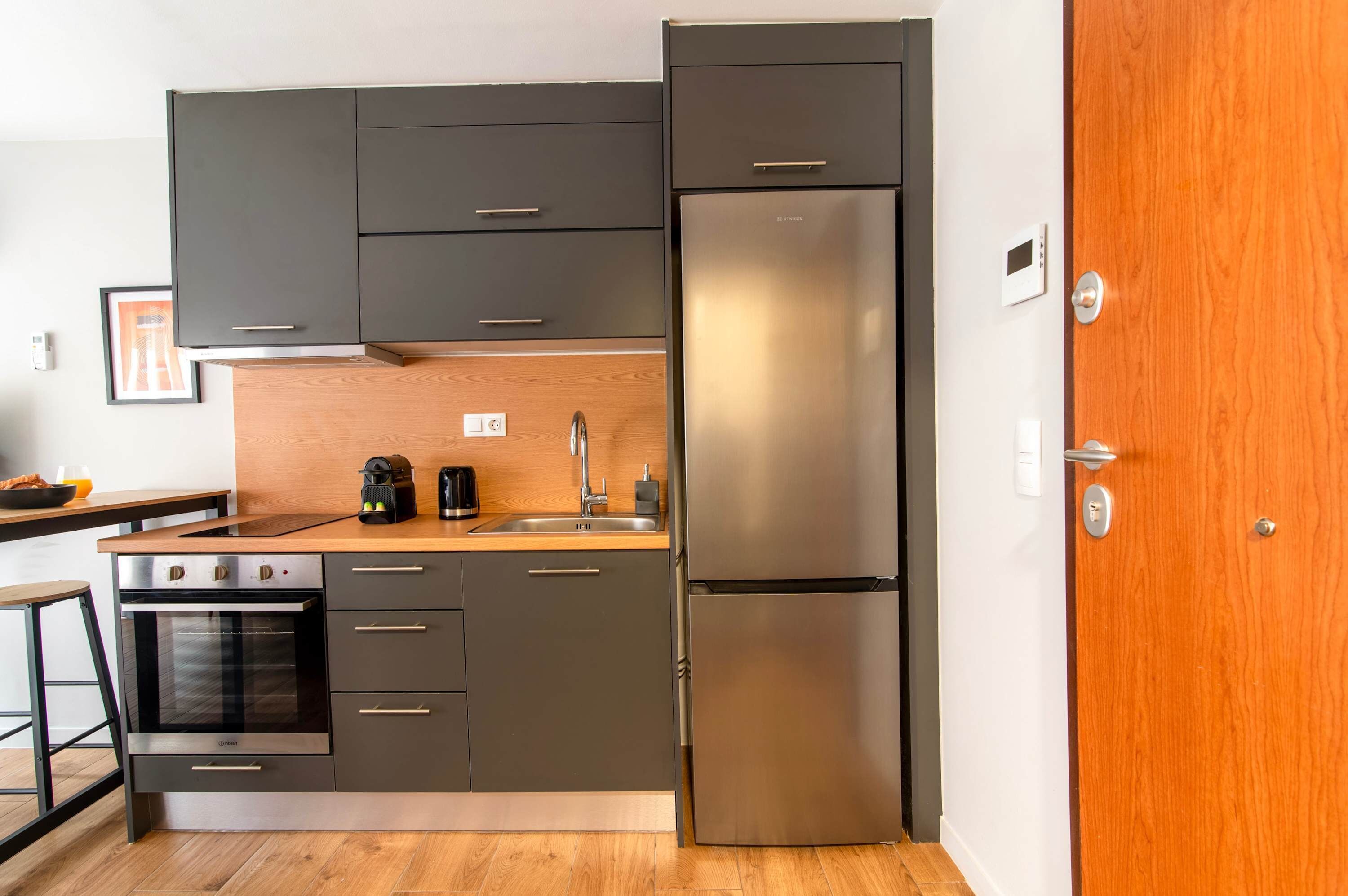 Eine moderne Küche mit dunklen Schränken, einem Edelstahlkühlschrank, einem eingebauten Backofen und einer Holzarbeitsplatte.