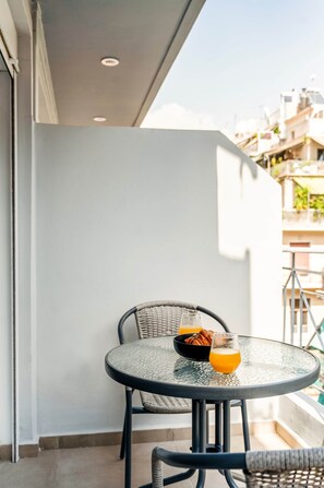 Ein Balkon mit einem runden Glastisch, einem Korbstuhl und einer Schale Gebäck.
