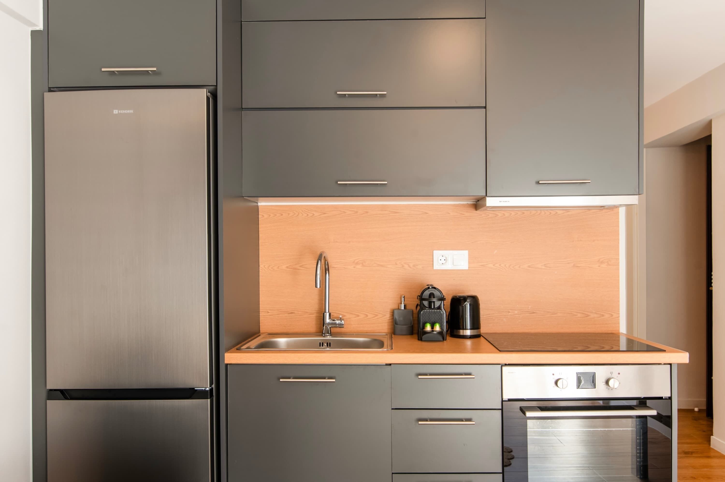 Een moderne keuken met grijze kastjes, een roestvrijstalen koelkast, een spoelbak en een koffiezetapparaat.