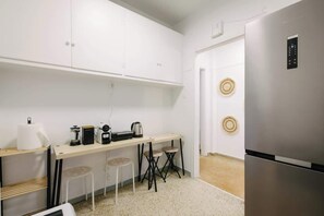 A compact kitchen with a stainless steel refrigerator, a wooden table with bar stools, and a white countertop. - Zen Sofokleous, Psirri (Athens City)