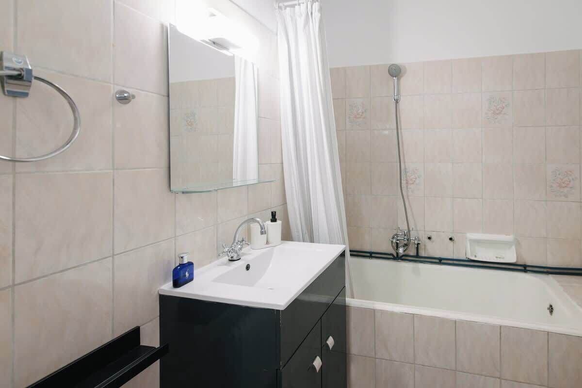 A modern bathroom with a white sink, black cabinet, and a glass-enclosed bathtub.