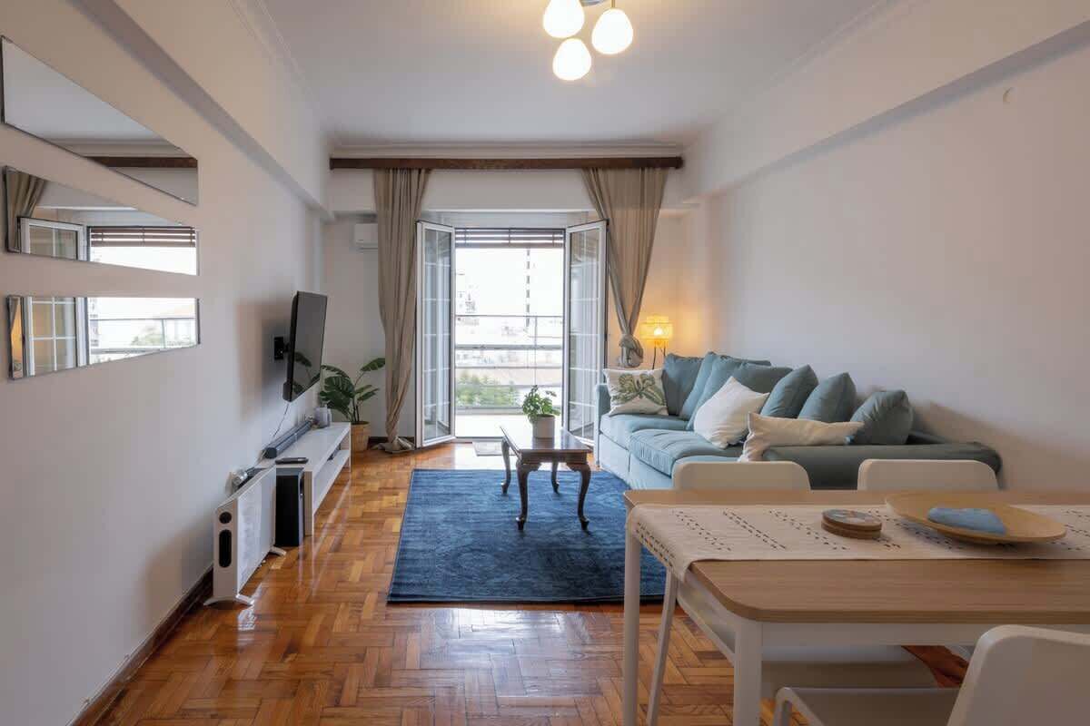 A modern living room with a sofa, a TV, a dining table, and a view through a glass door.