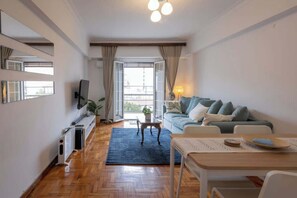 A modern living room with a sofa, a TV, a dining table, and a view through a glass door. - Zen Sofokleous, Psirri (Athens City)