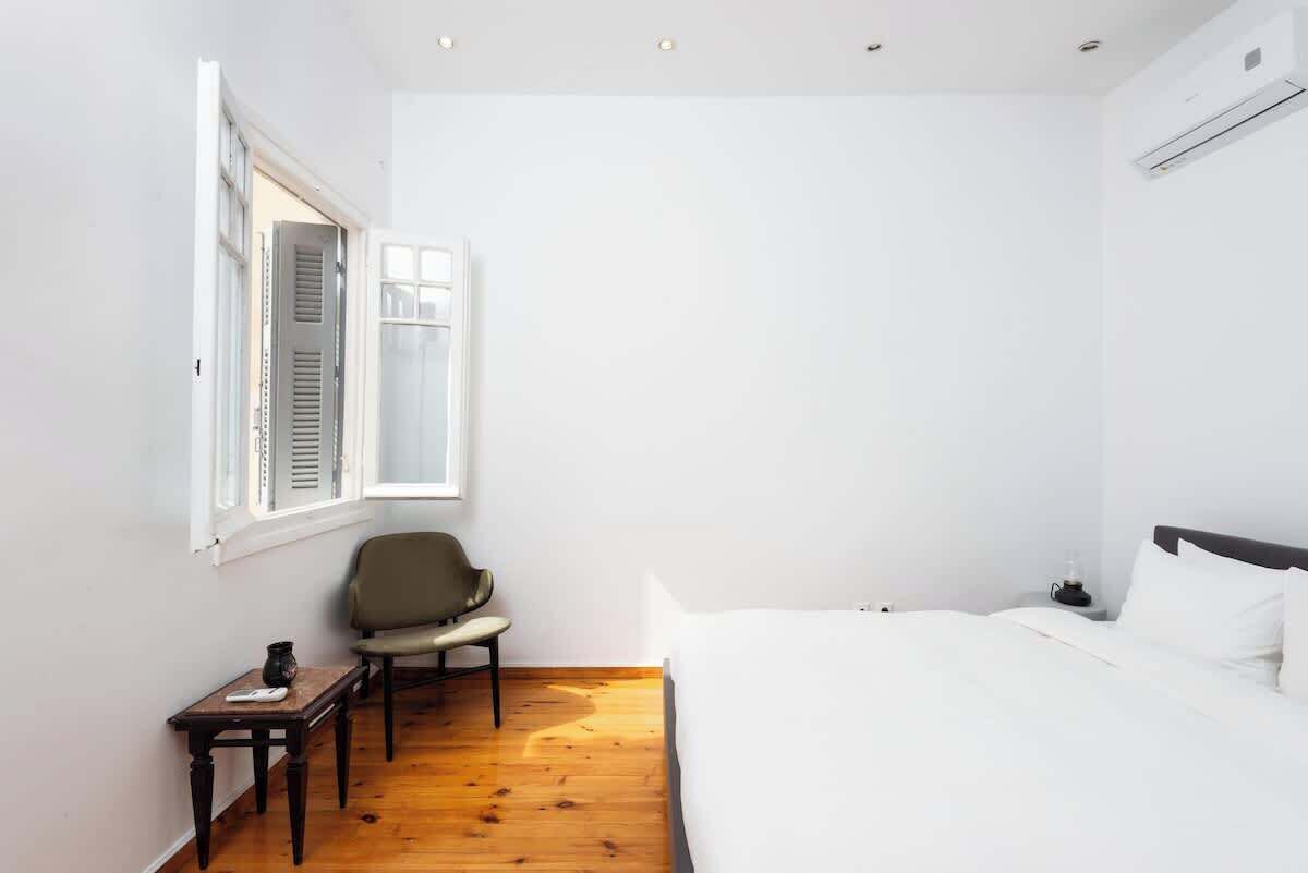 A bedroom with a bed, a chair, a small table, and a window with shutters.