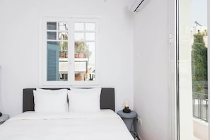 Ein Schlafzimmer mit Bett, Fenster, Nachttisch und Blick ins Freie.