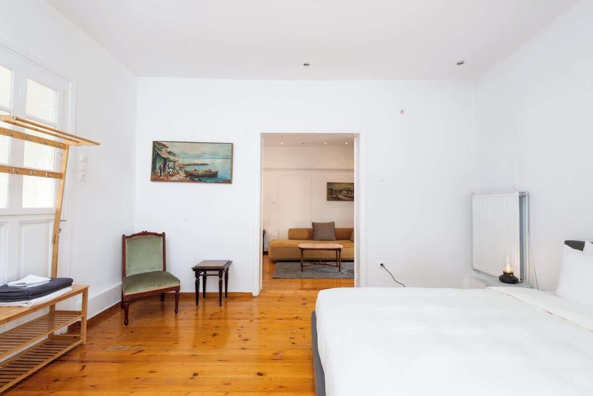 Un dormitorio con cama, una silla, una mesita y un cuadro en la pared.