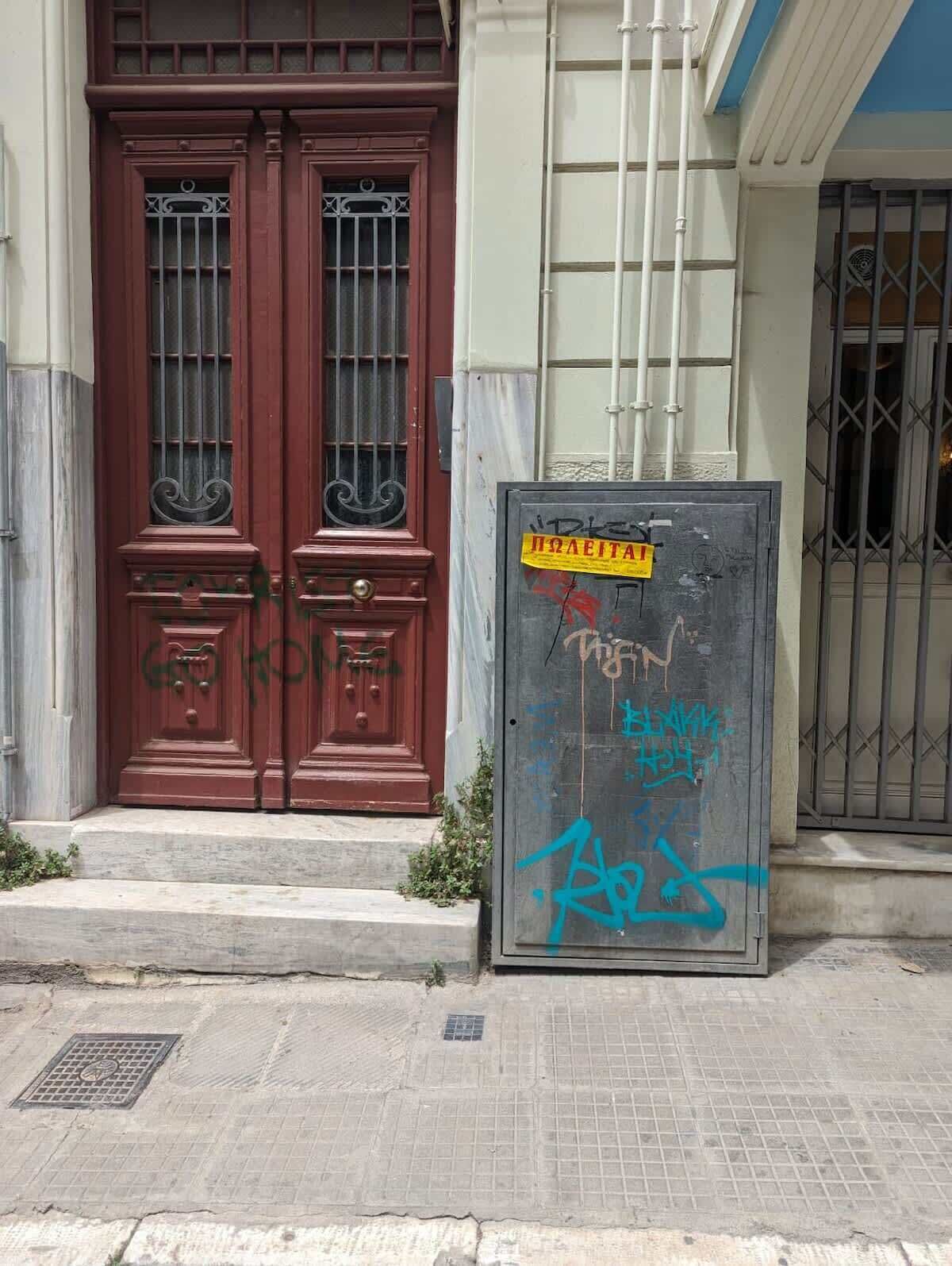 Un edificio con un'imponente porta rossa doppia, un cancello in metallo e uno stanzino con graffiti.