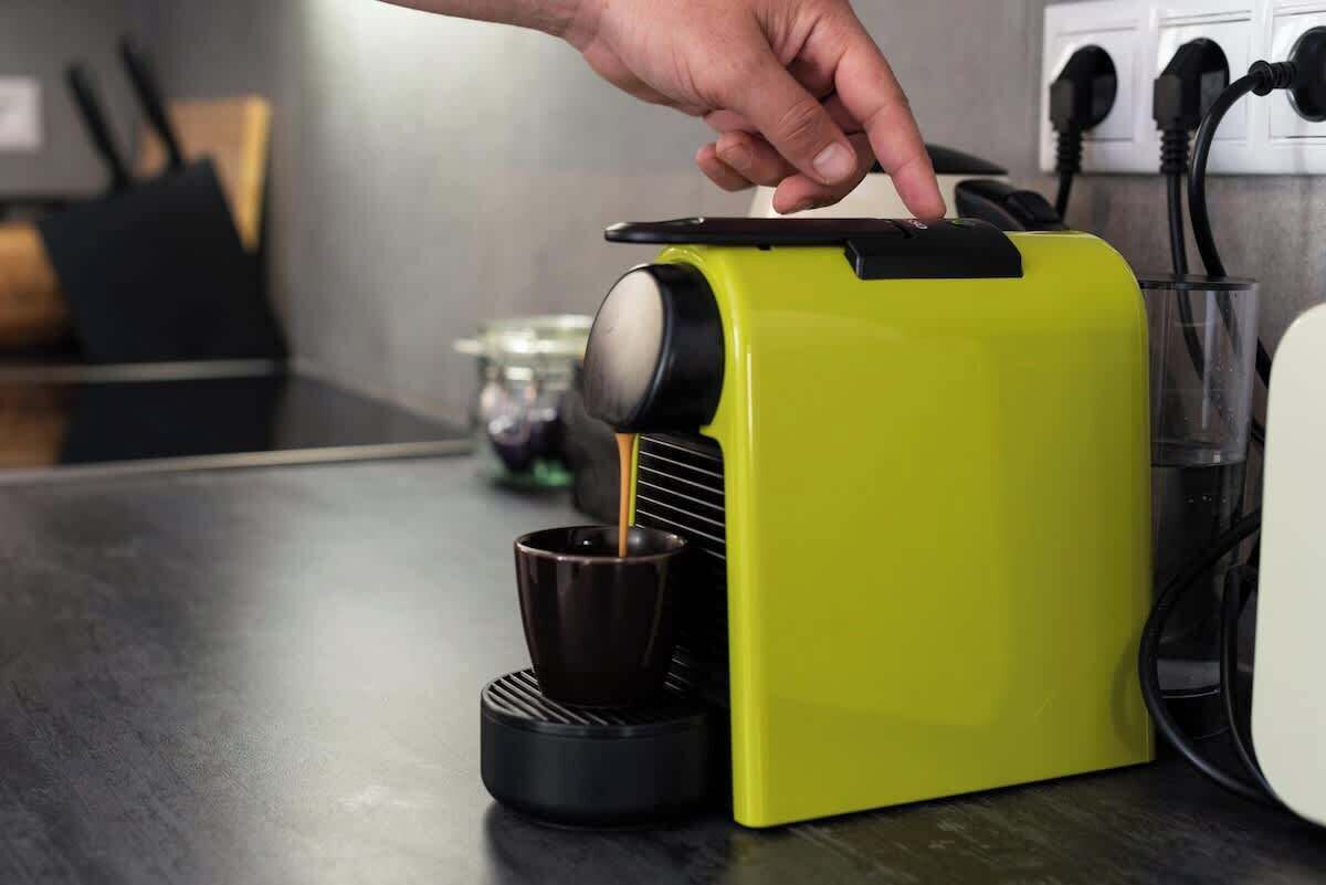 A hand pressing a button on a coffee machine, with a cup of coffee being dispensed into a black cup.