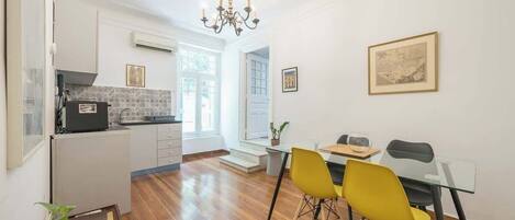 A modern kitchen with a built-in oven, a dining area with a glass table and chairs, and a chandelier.