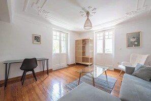 A room with a glass table, a black chair, a grey sofa, a wooden floor, and a white ceiling with decorative moldings. - Zen Amazing, Exarchia (Athens)