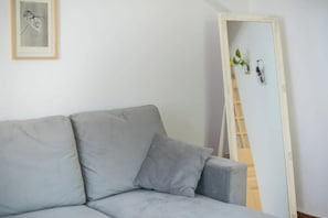 A grey sofa with a cushion, a framed picture on the wall, and a mirror leaning against the wall. - Zen Amazing, Exarchia (Athens)