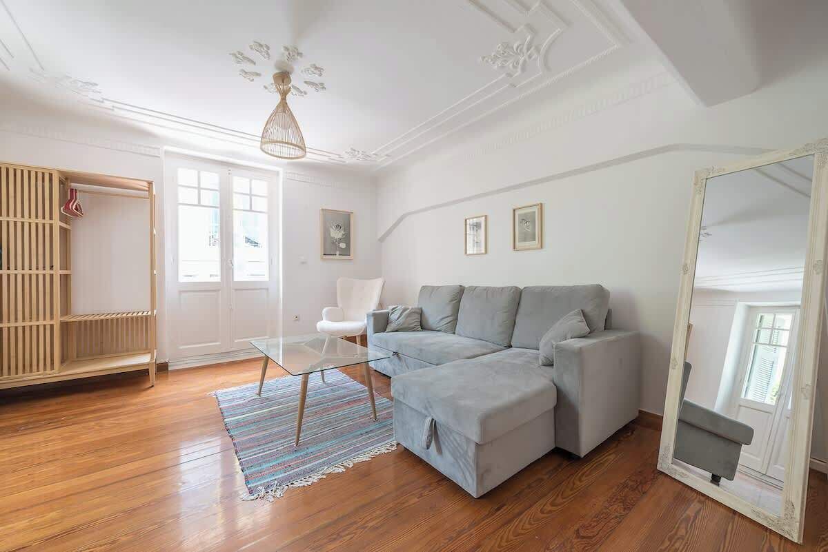 A modern living room with a grey sofa, a glass coffee table, a wooden floor, and a white ceiling with decorative molding.