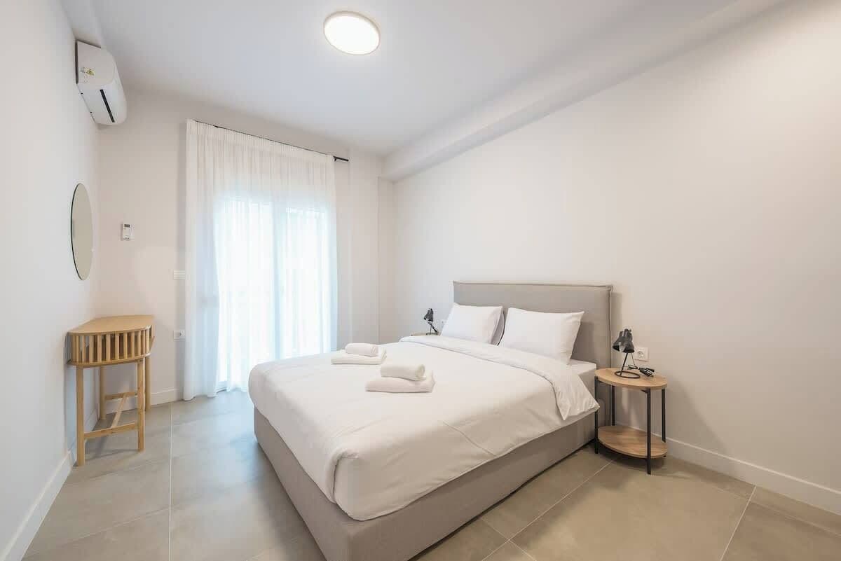 A bedroom with a bed, a bedside table, a lamp, and a window with curtains.