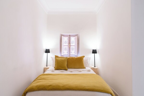 Ein Schlafzimmer mit einem Bett, zwei Nachttischlampen, einem Fenster mit dekorierter Scheibe und einer Deckenleuchte.