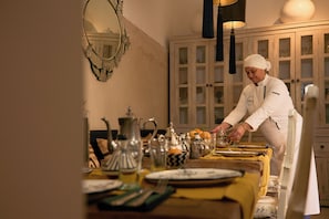 Ein Koch bereitet Essen in einer Küche mit Holdelementen und einem Esszimmer mit Geschirr und Besteck.