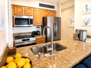 A modern kitchen with granite countertops, stainless steel appliances, and wooden cabinets. - Mahana Villas | Oceanfront 2 Bedroom Sleeps 5 | Car Incl. w/ 6+ Nights | MAH ML-4196 by KBM (Lahaina)